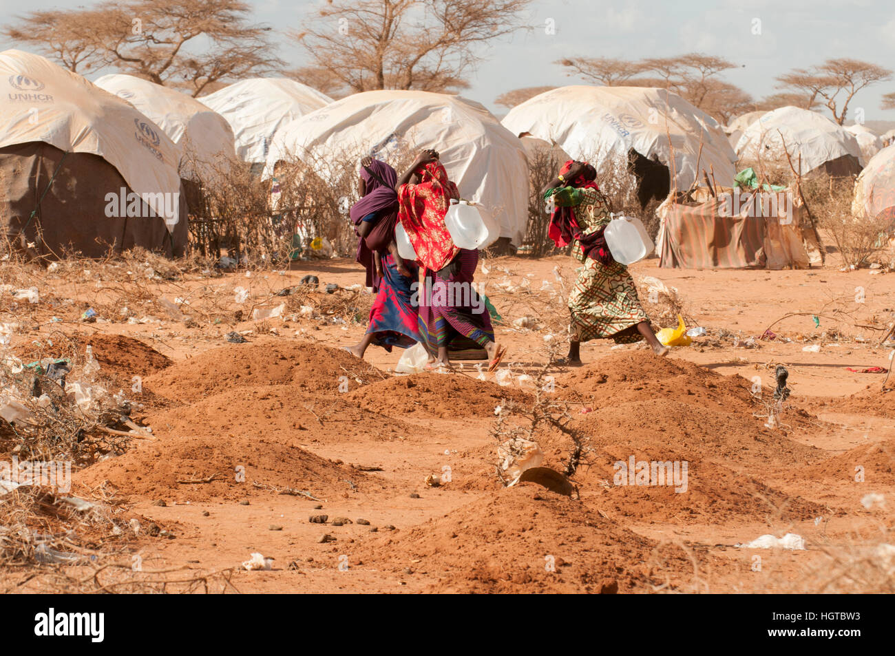 Somalian living in makeshift shelters walking past a graveyard at the Dadaab refugee camp on the border of Somalia and Kenya. Stock Photo