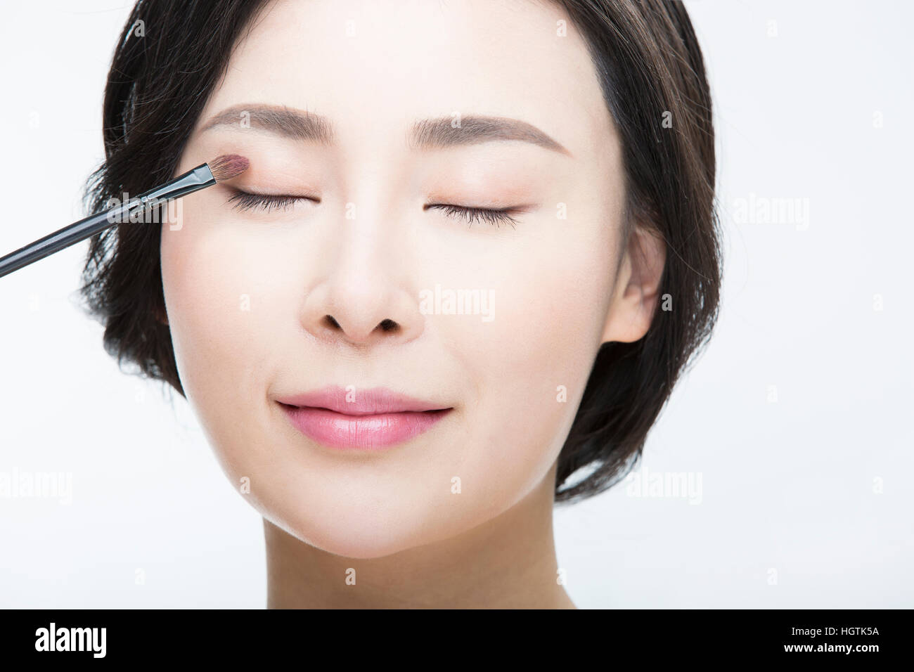 Portrait of young woman putting on makeup with her eyes closed Stock Photo