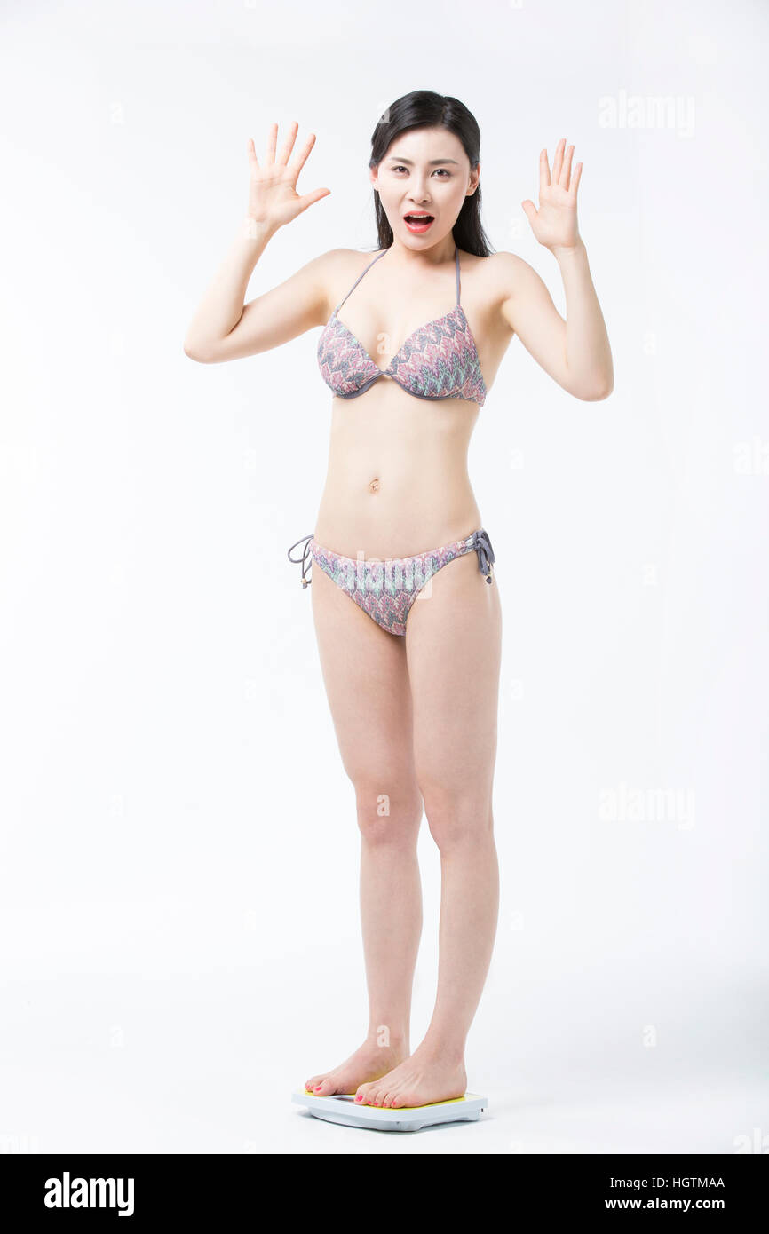 Young woman in bikini standing on a scale surprised Stock Photo - Alamy