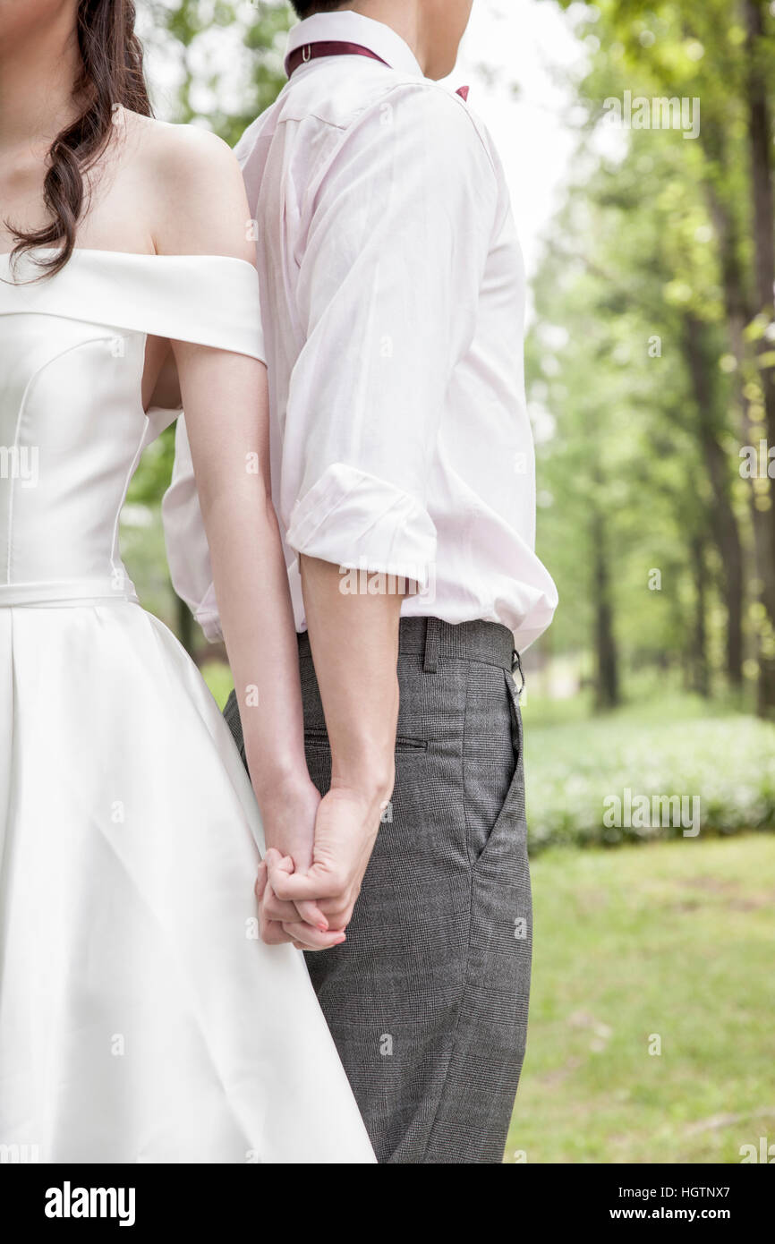 Side view of young wedding couple holding hands outdoors Stock Photo