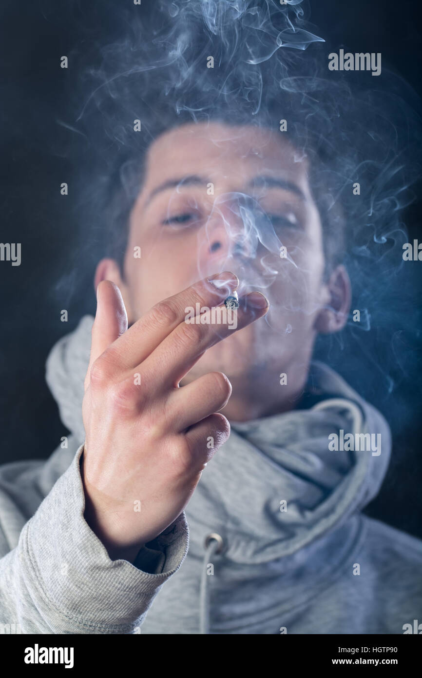cigarette smoke hood Hand holding smoking cigarette against hi-res stock photography and images