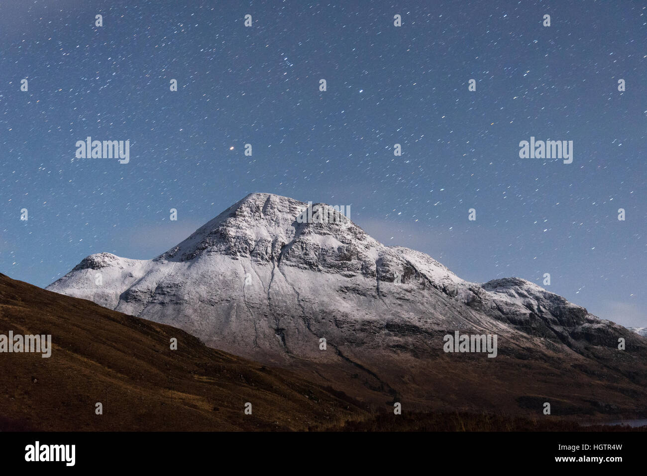 mountain illuminated by soft moonlight at night with snow and stars Stock Photo