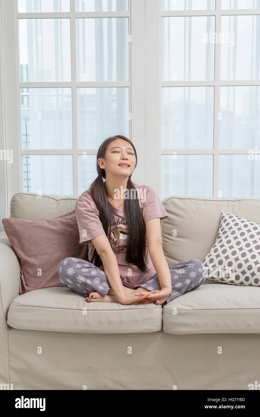 Young woman sitting on sofa closing eyes Stock Photo - Alamy