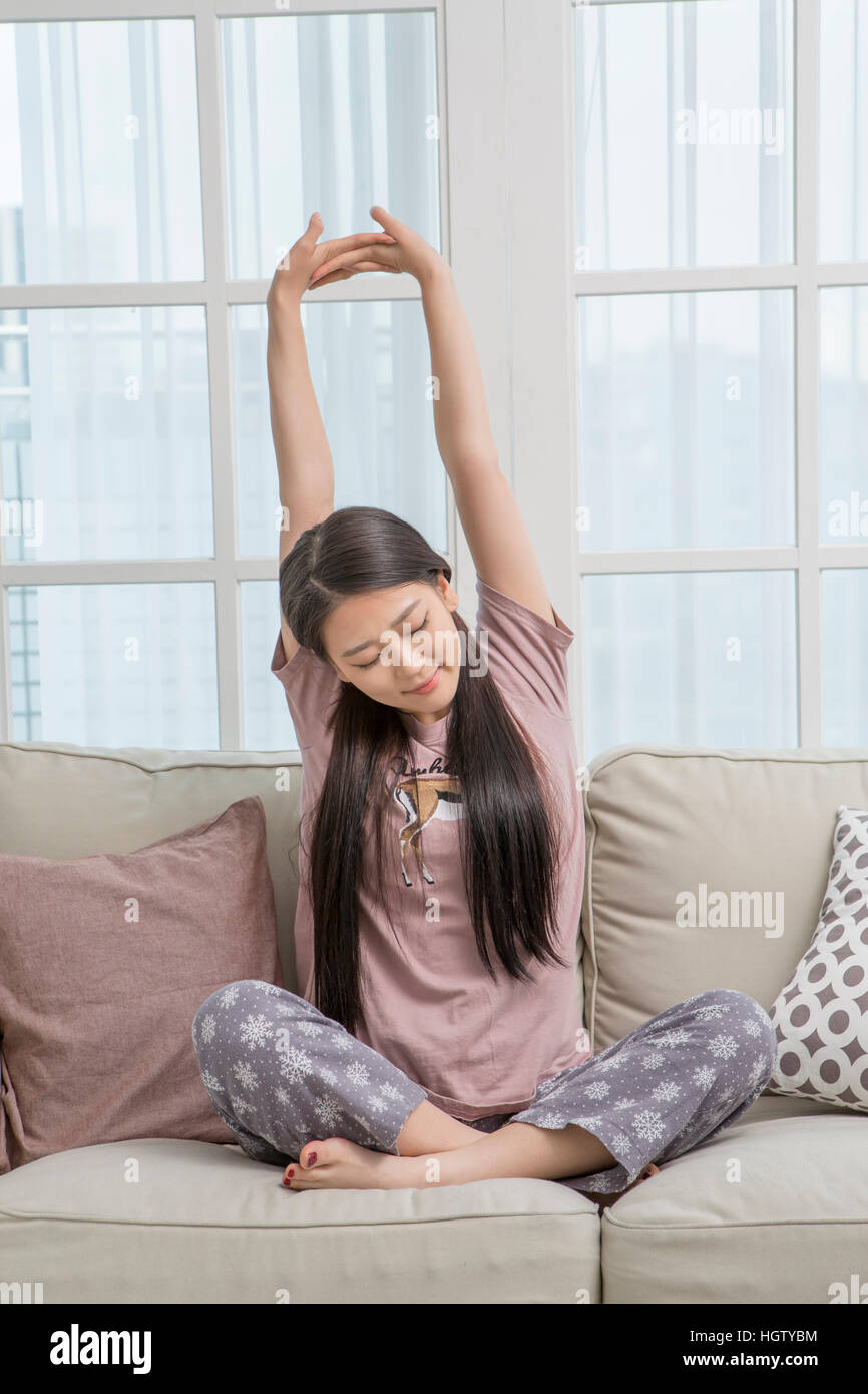 Young woman stretching sitting on sofa Stock Photo - Alamy