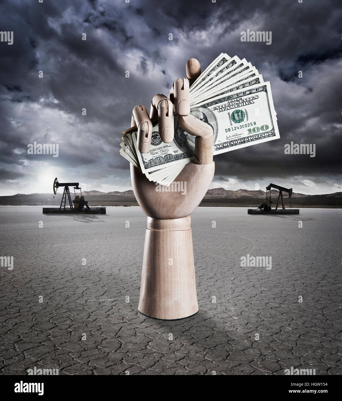 Manikin Hand Holding Money In Dry Lake Bed With Storm Clouds And Drilling Rigs In Background Stock Photo
