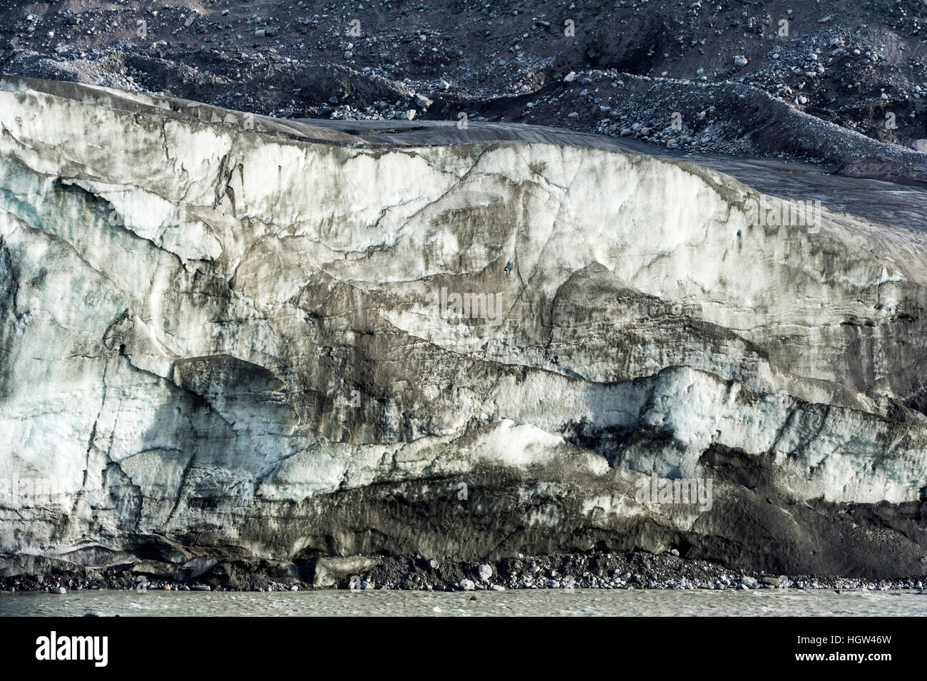 Erosion from ice against rock deposits silt and soil sediment on the edges of ice blades along the fracture zone of a glacier. Stock Photo