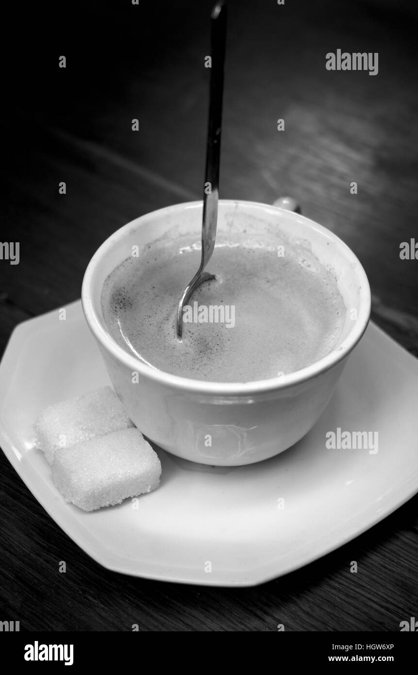 Very strong cup of coffee with spoon standing up in it (black and white