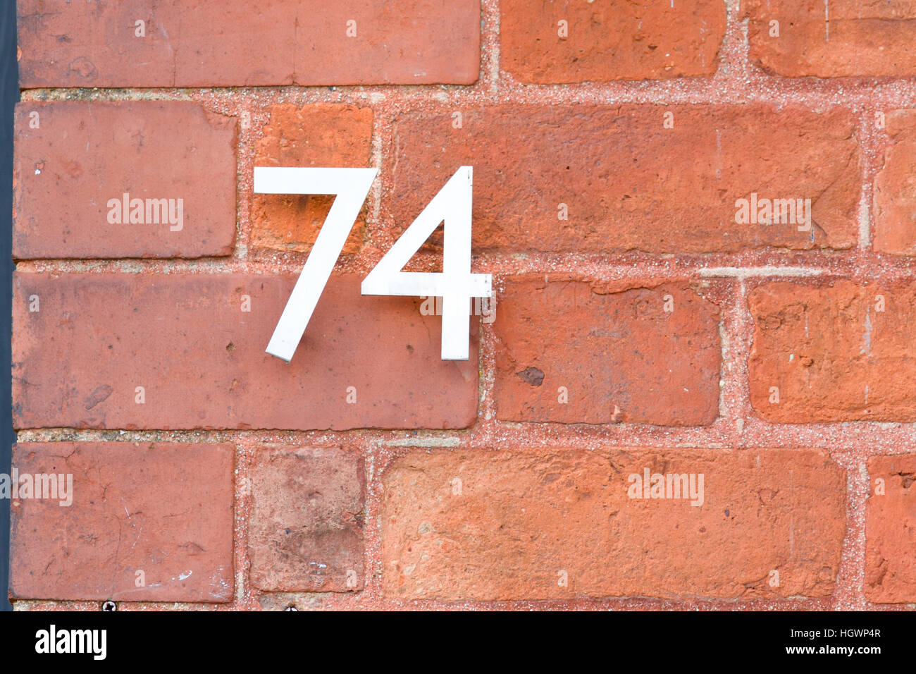 House Number 74 sign on red brick wall Stock Photo
