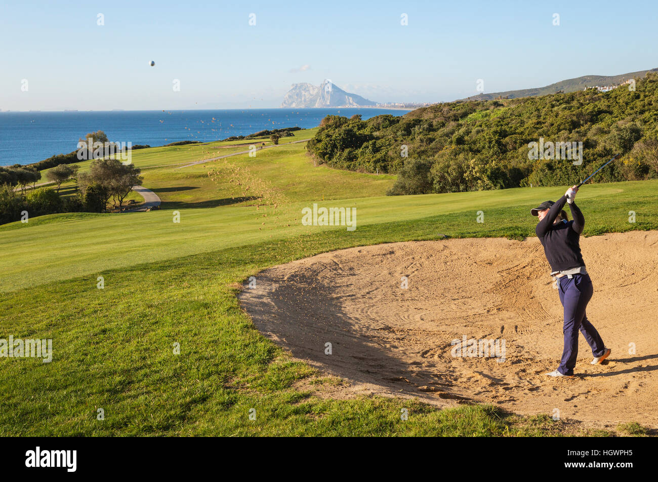 Golfer hitting from bunker at La Alcaidesa Golf Resort with Mediterranean Sea and Rock of Gibraltar, Cádiz, Andalusia, Spain Stock Photo