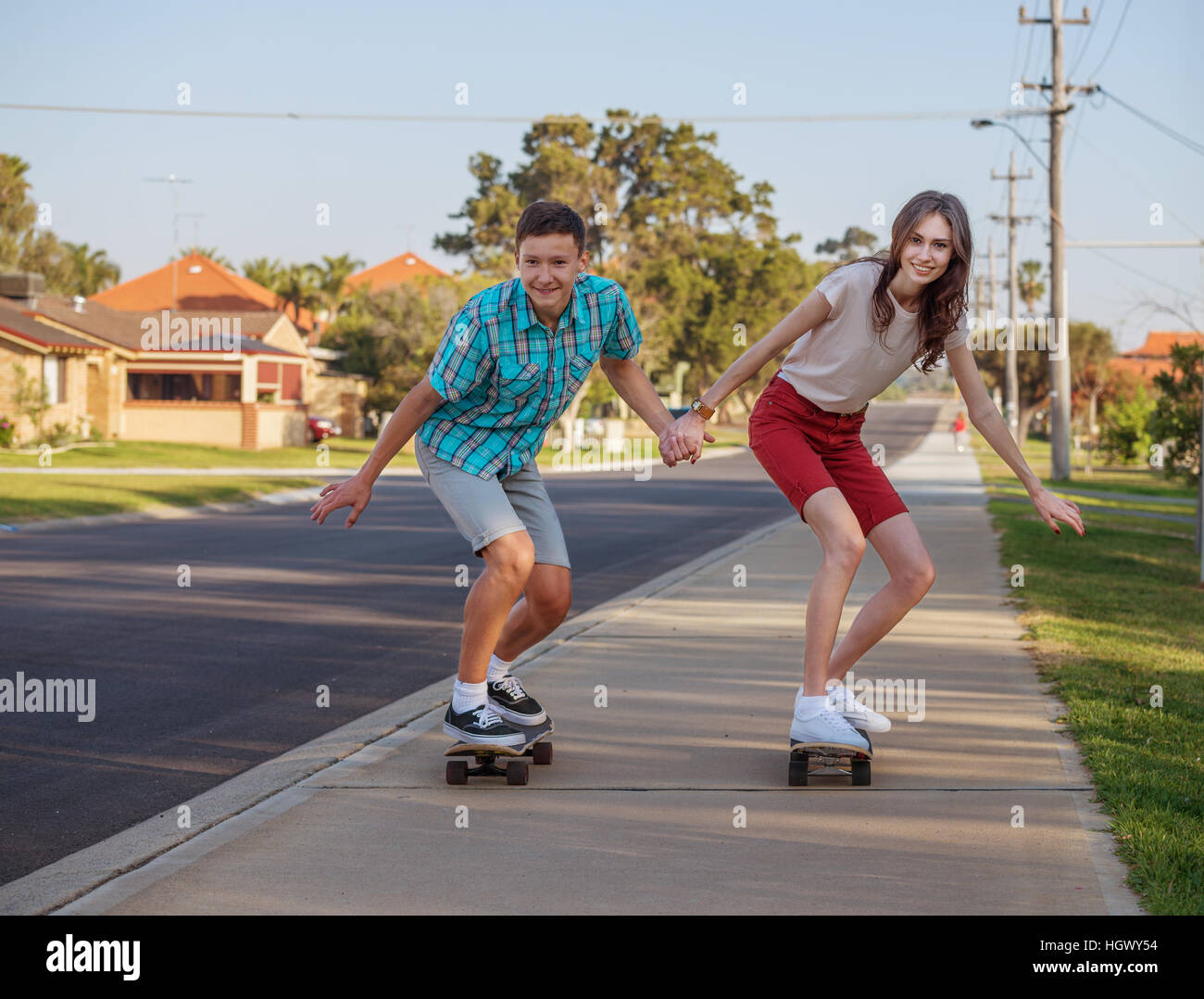 Happy brother and sister having fun with  skateboard on the street in the evening light Stock Photo