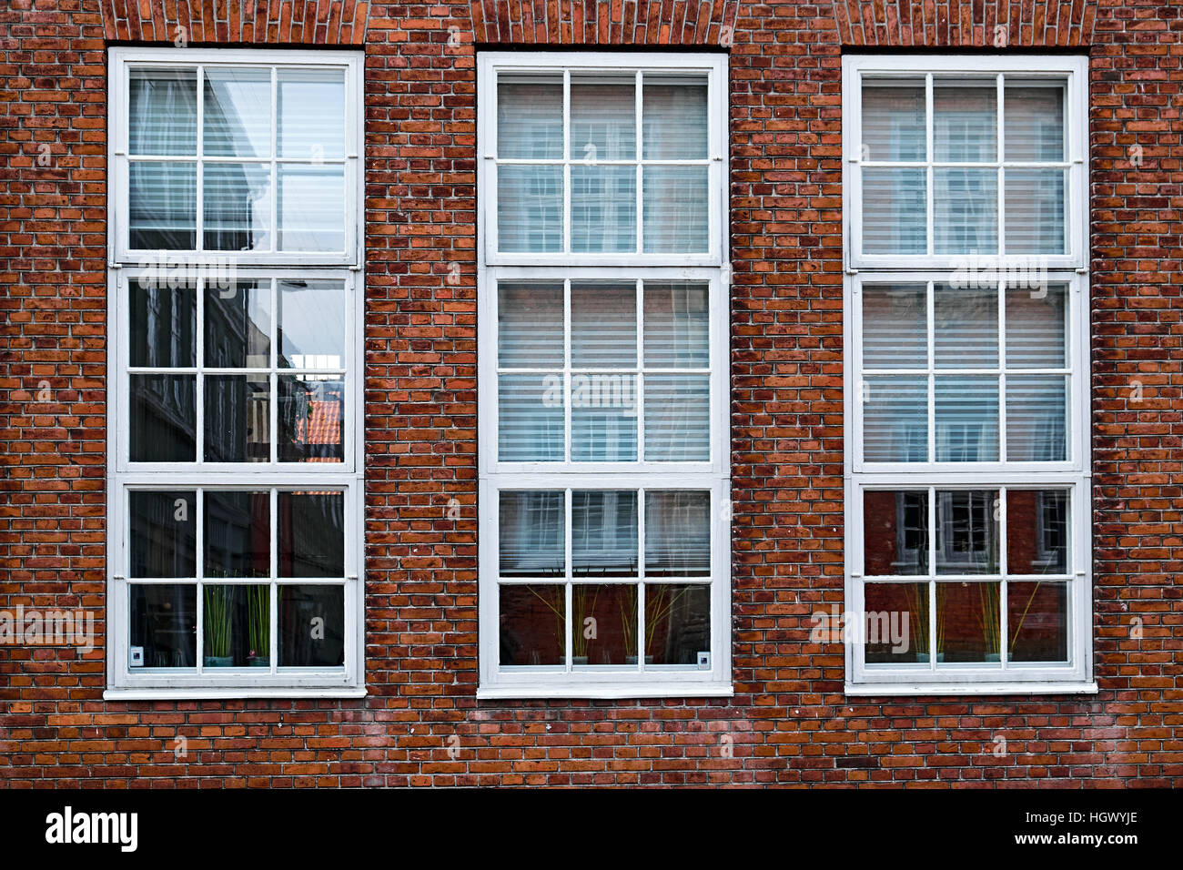 Three tall, white painted, wood windows in a red masonry brick facade Stock Photo