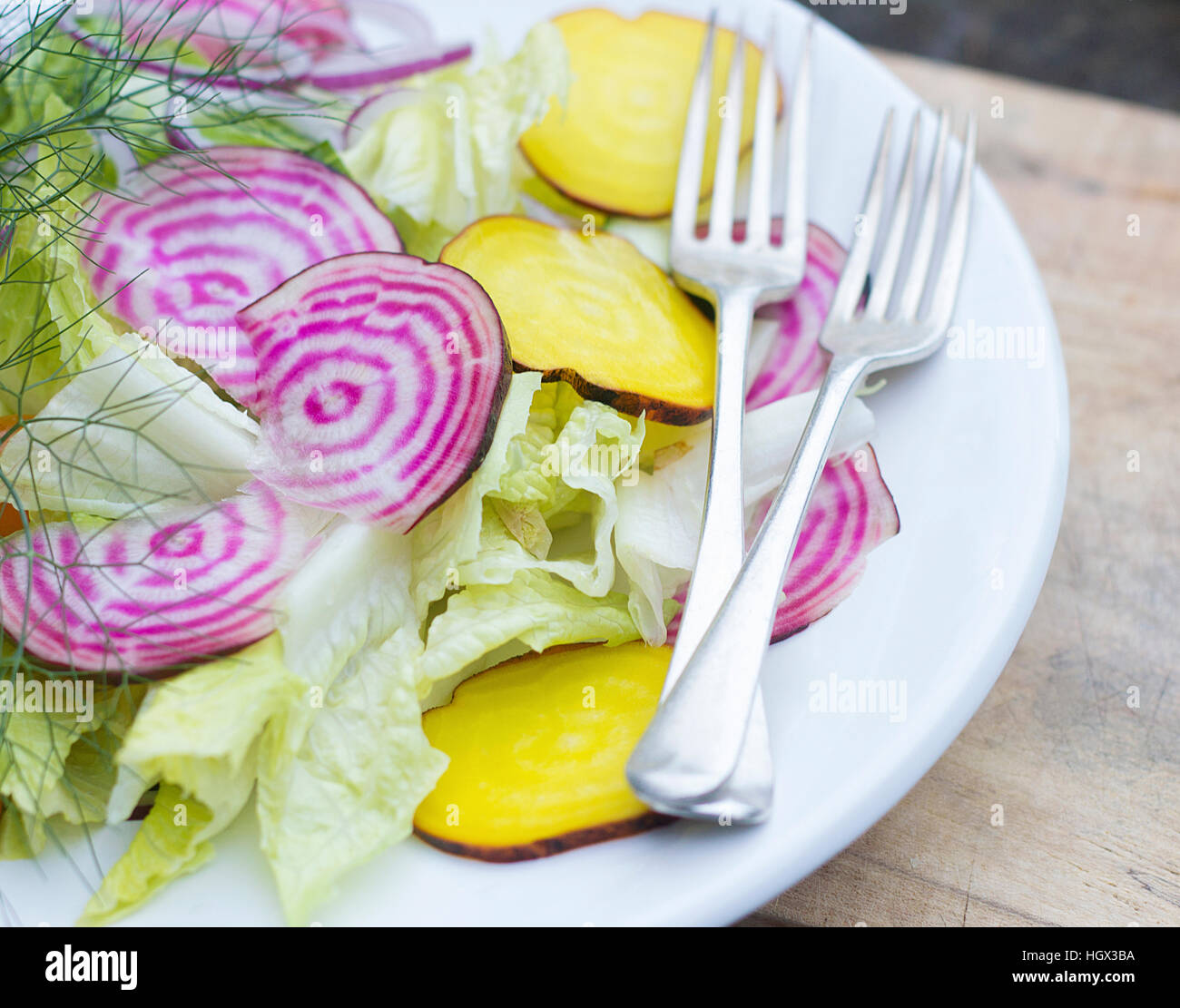 Purple and yellow beetroot salad with antique cutlery on white plate, wooden board. Stock Photo