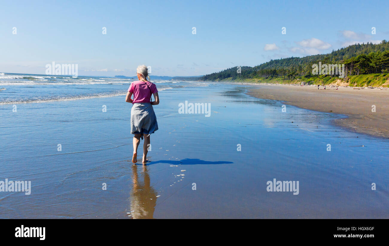 Woman walking on beach at Kalaloch Beach, Olympic National Park, Washington State, USA.  Low tide, blue skies, empty beaches. Stock Photo
