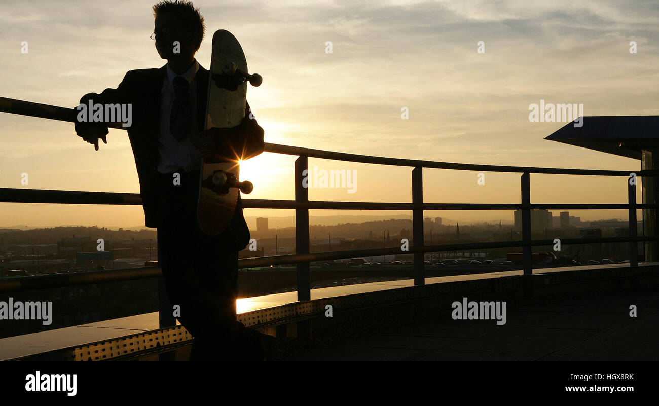 Boy holding skateboard in silhouette against city landscape Stock Photo