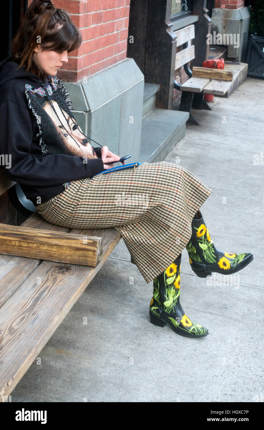 Stylish young woman in ornate cowboy boots and designer hoodie using her  cellphone on a bench in Soho in New York City Stock Photo - Alamy