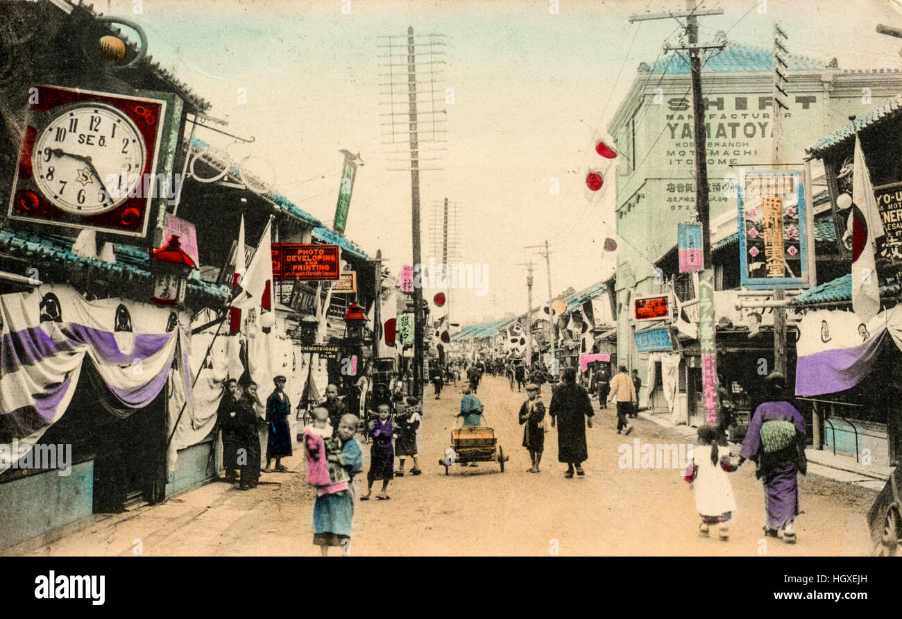 Japan, Motomachi, Kobe. Vintage postcard hand coloured. Main street scene, stores n both sides, people and carts in road. Circa 1910. Stock Photo
