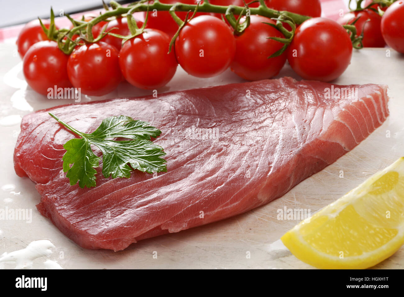 Crop view of raw tuna fillet piece with cherry tomatoes and lemon on the table surface Stock Photo