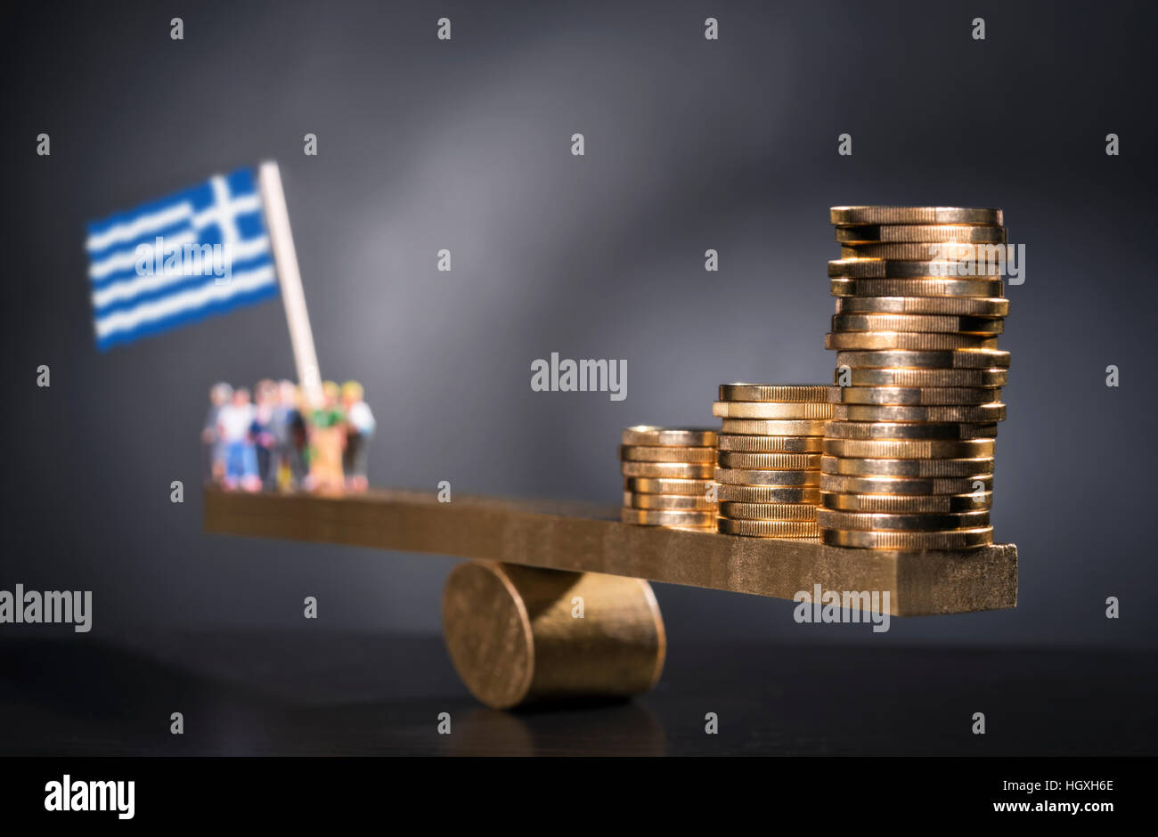 Seesaw with coins on one side and a group of people with the Greek flag on the other side. Stock Photo