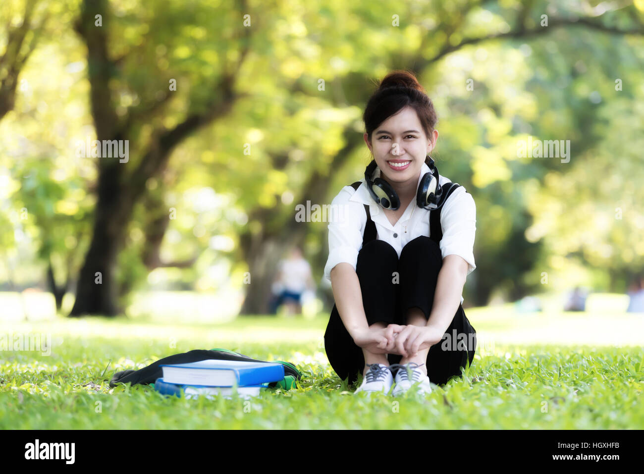 Asian female student girl outside in park listening to music on headphones while studying Stock Photo