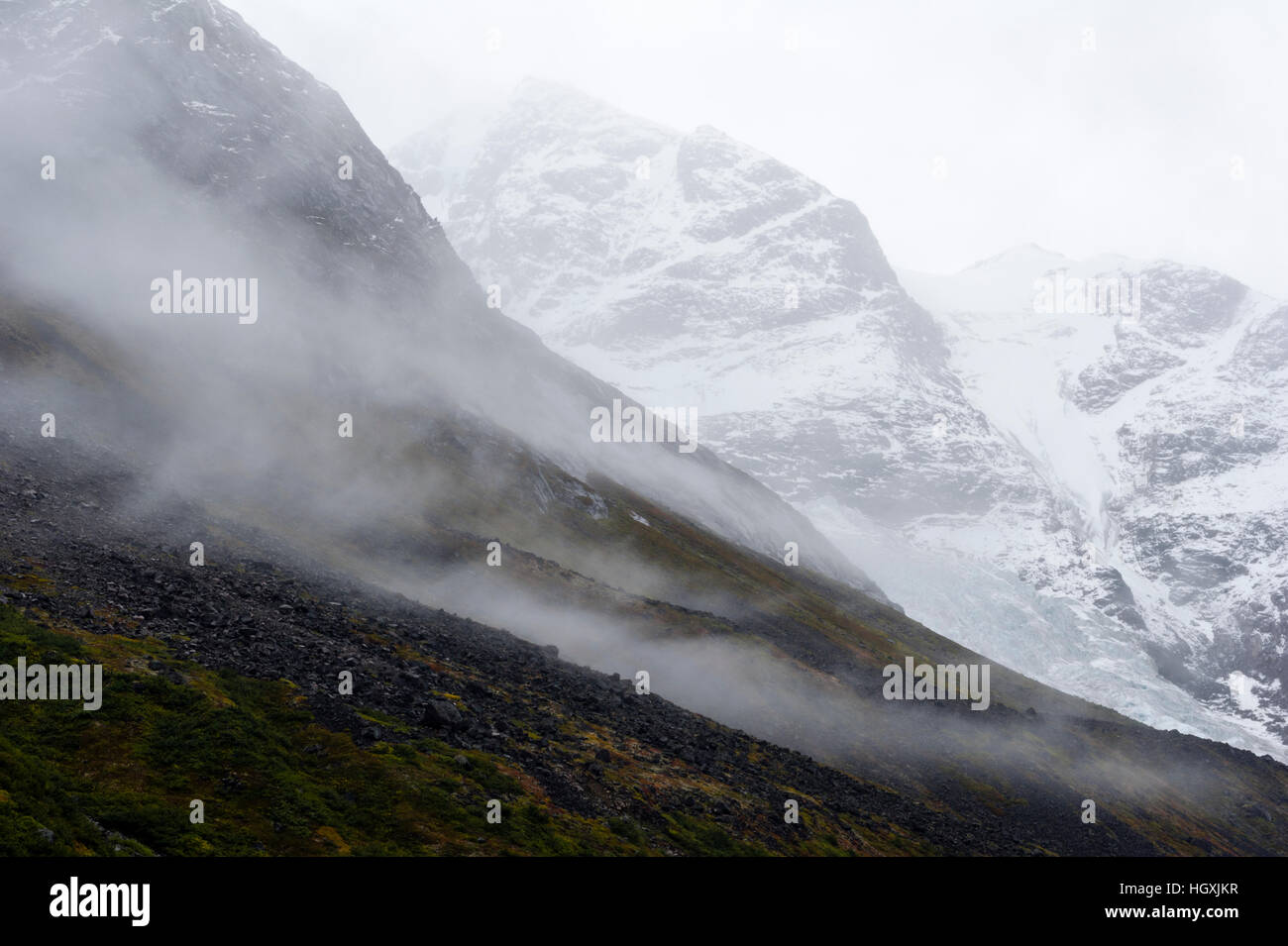 Cloud and mist shroud jagged and rugged mountain peaks during a rain storm in a fiord. Stock Photo