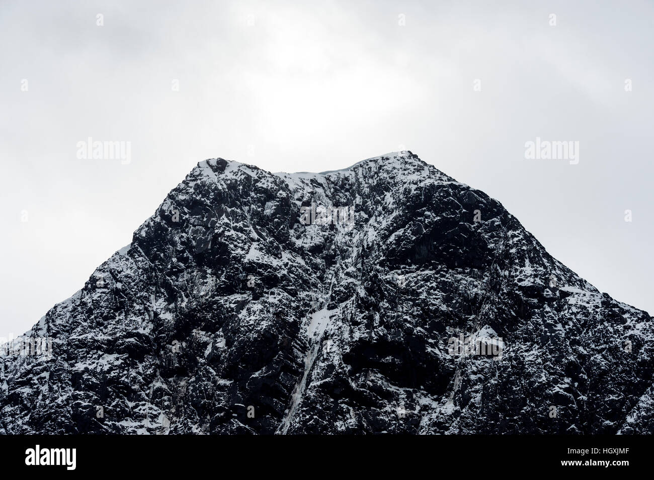 A rugged cone-shaped mountain summit dusted in snow and ice. Stock Photo