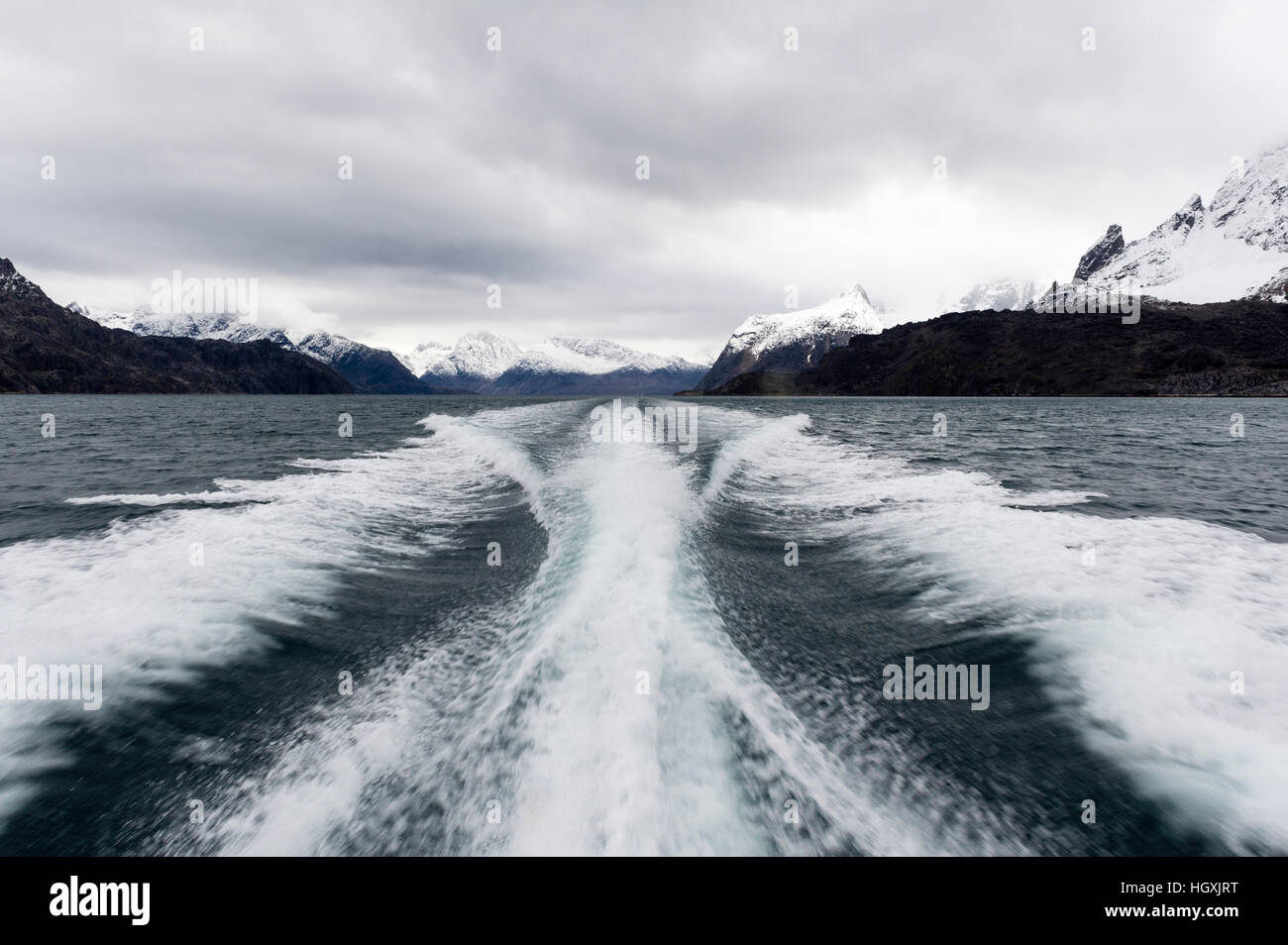 A boats wake peels between snow covered peaks in a fjord. Stock Photo