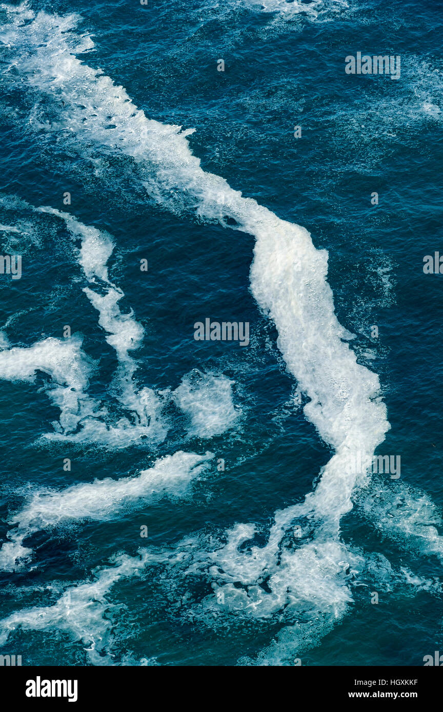 Wave foam trapped in currents along the base of coastal cliffs. Stock Photo