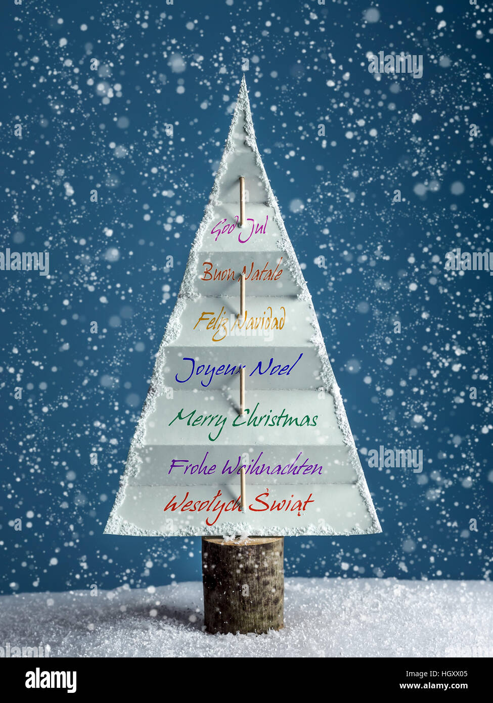 Paper christmas tree with International seasonal greetings over dark blue background with snowing effect Stock Photo