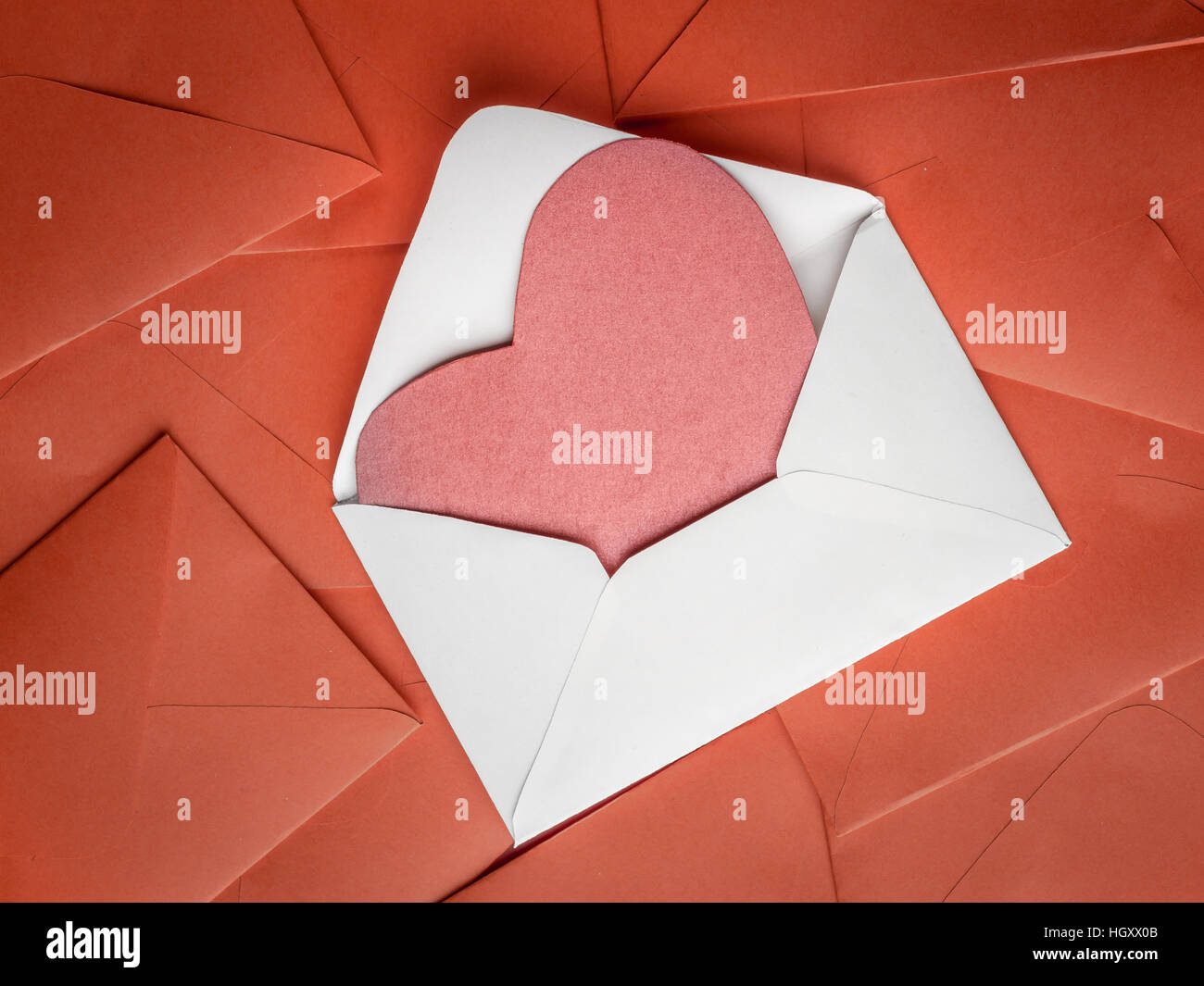 White envelope with red paper heart insert placed on pile of red envelopes Stock Photo