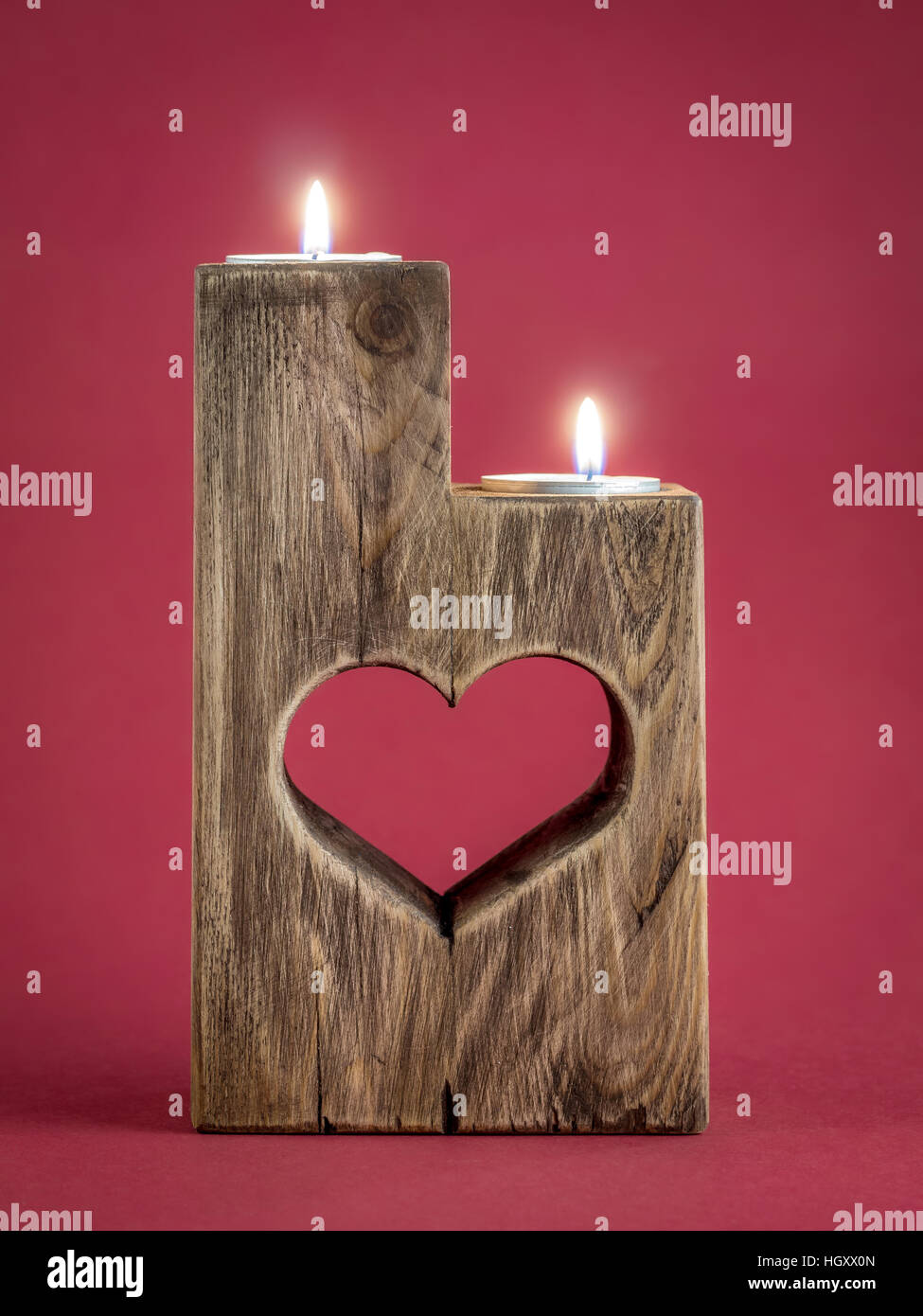 Lit romantic wooden candle holder with cut heart over red background Stock Photo