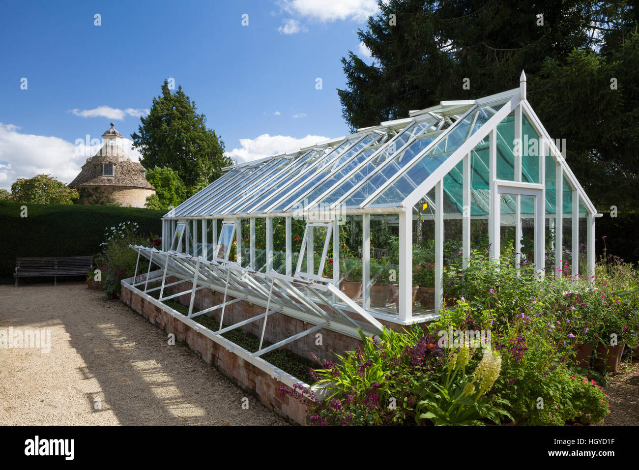 The greenhouse and open coldframe with stone dovecote beyond within the