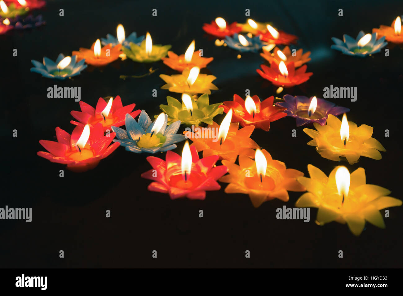 Close focus on colorful candles with fire floating on oil pool in low key tone. People float candles for lucky wishing. Stock Photo