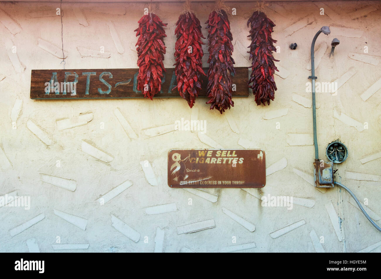 Dried chiles and a vintage cigarette sign against a colorfully patterned wall in Chimayó, New Mexico, USA Stock Photo