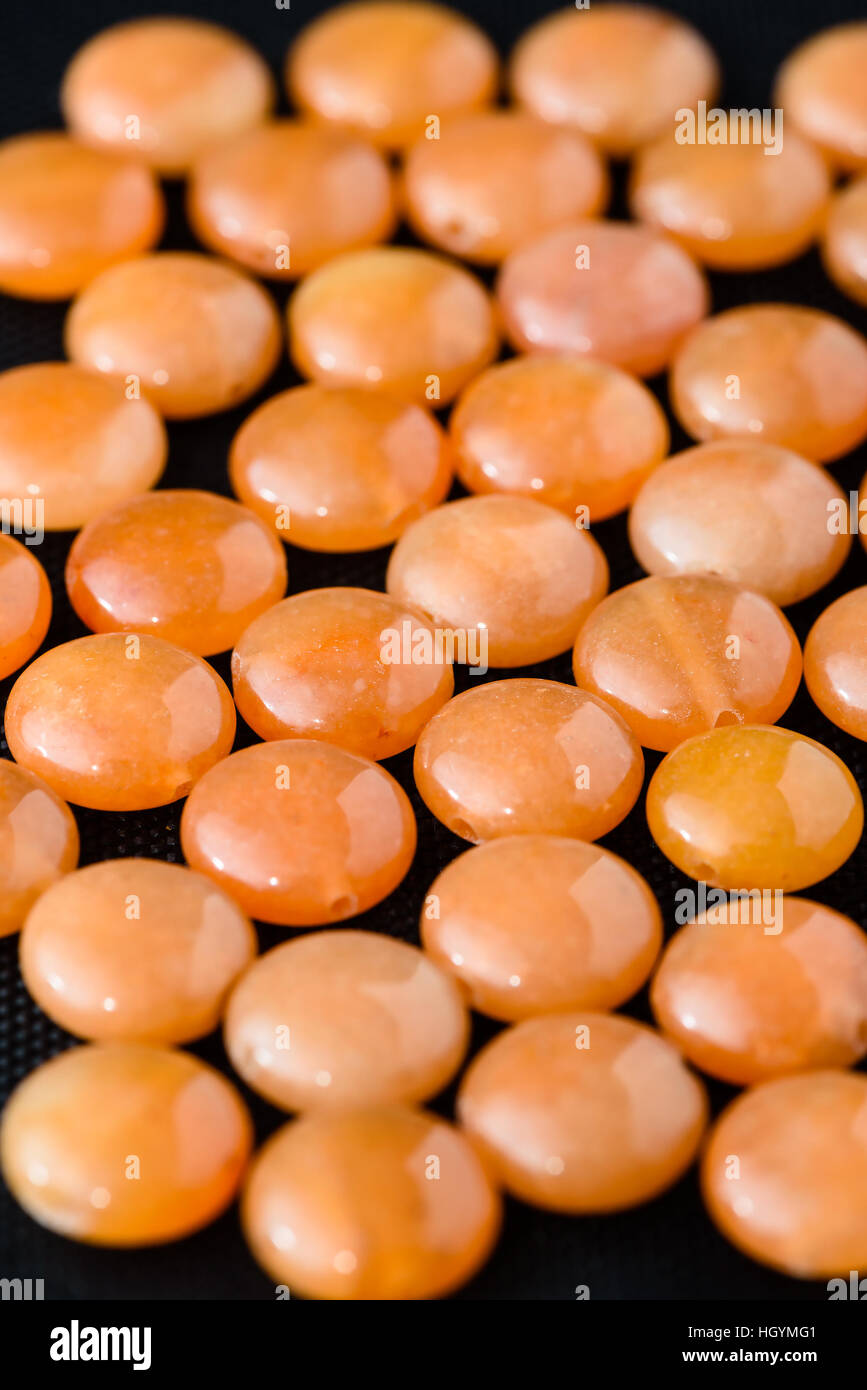 Collection of orange aventurine coin beads on black weave. Stock Photo