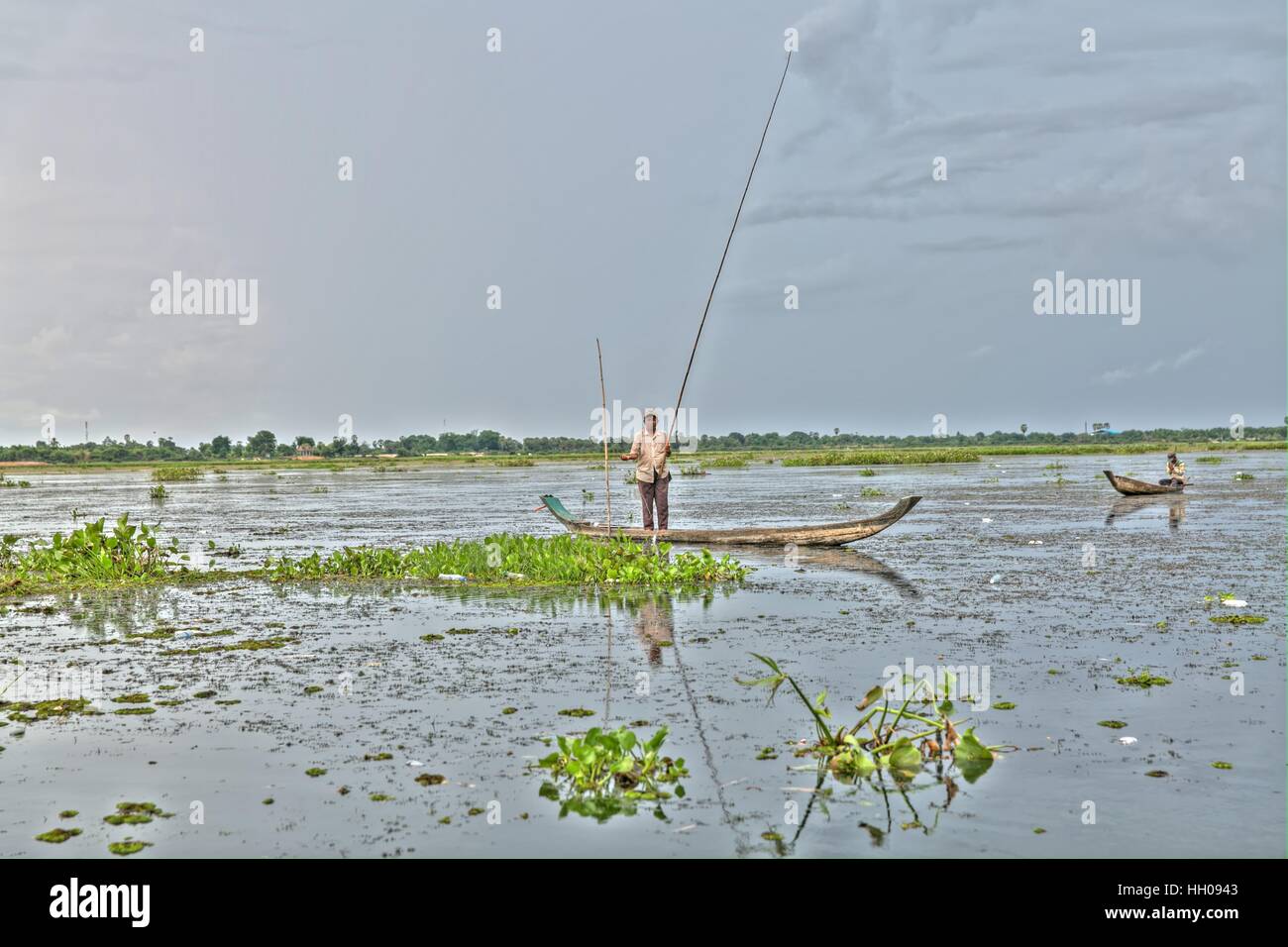 This is an idyllic scene with a fisherman standing in his boat fishing on Tonle (lake) Bati, Phnom Penh, Cambodia. Stock Photo