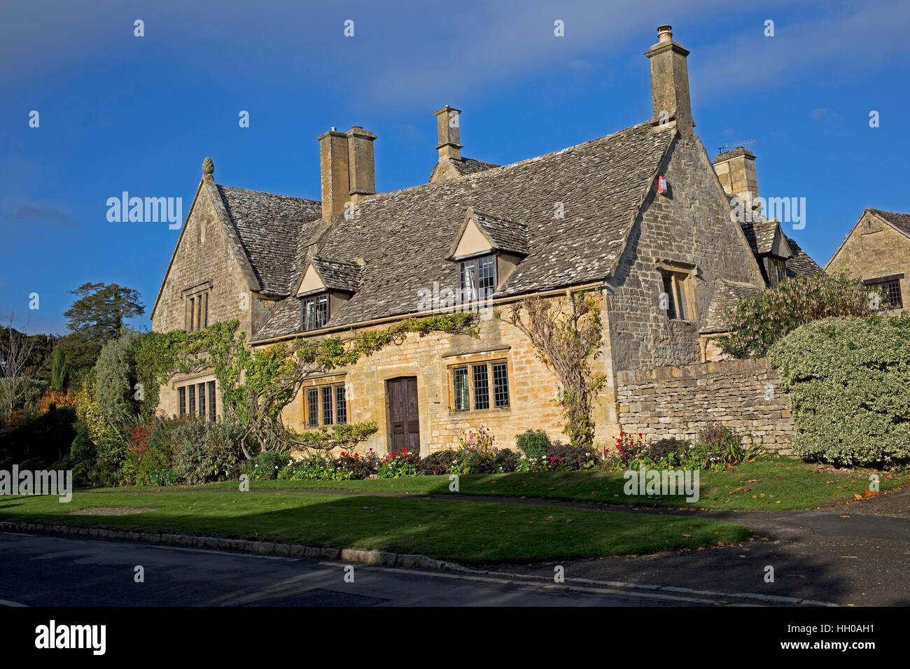 Attractive Cotswold stone cottage with stone tiles mullion windows sunlit against blue sky Chipping Campden UK Stock Photo