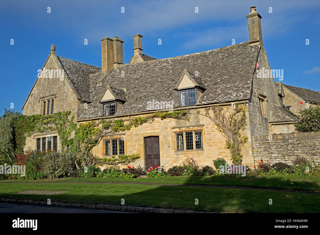 Attractive Cotswold stone cottage with stone tiles mullion windows sunlit against blue sky Chipping Campden UK Stock Photo