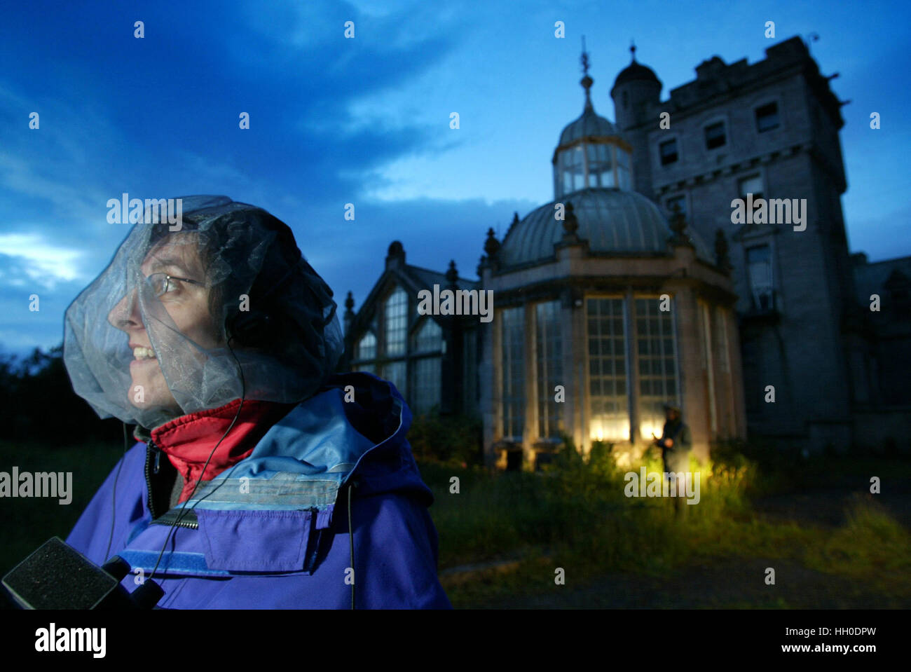 woman, wearing protective net for insects, out bat watching with spooky abandoned house in background Stock Photo