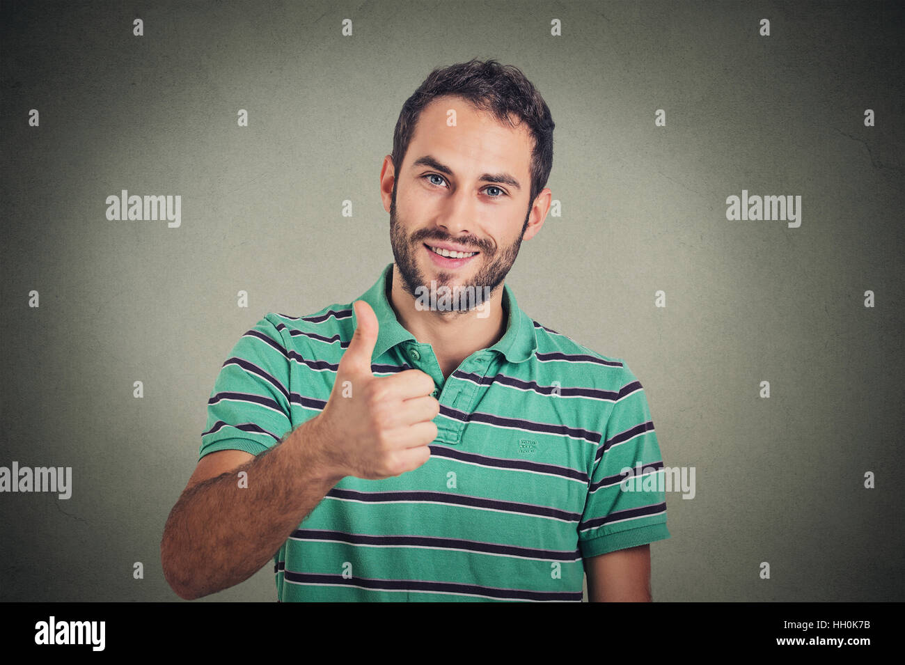 Happy man giving thumbs up sign isolated on gray wall background. Positive human face expression body language Stock Photo