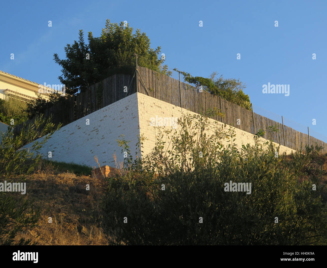 Corner of white painted brick retaining wall on steep hillside Stock Photo