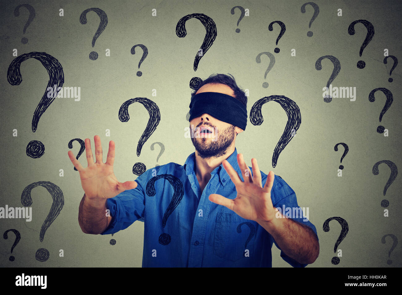 Portrait business man blindfolded stretching his arms out walking through many questions isolated on gray wall background Stock Photo