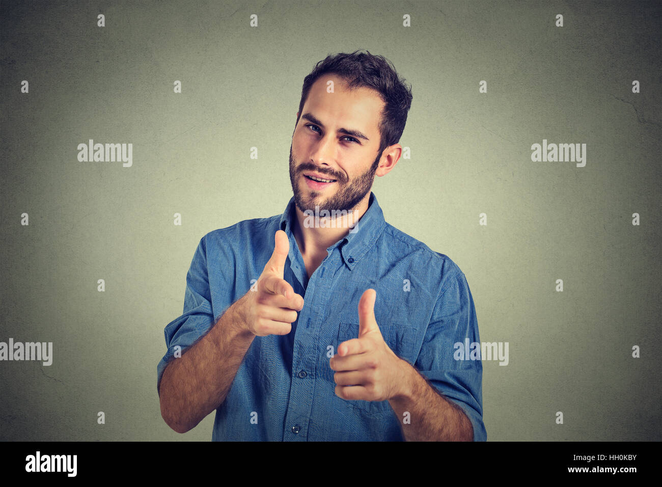 handsome young smiling man giving thumbs up pointing fingers at camera, picking you as friend isolated on gray background Stock Photo