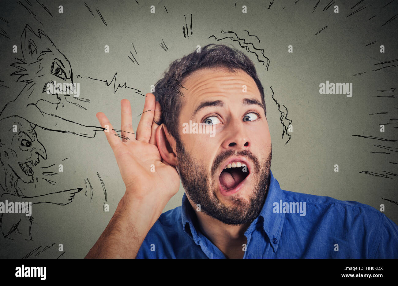 man with hand to ear gesture and evil voices screaming blaming him isolated on gray background. Human emotion face expression Stock Photo