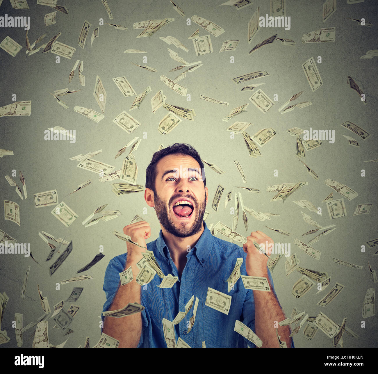 happy man exults pumping fists celebrates success screaming under money rain falling down dollar bills isolated gray background Stock Photo