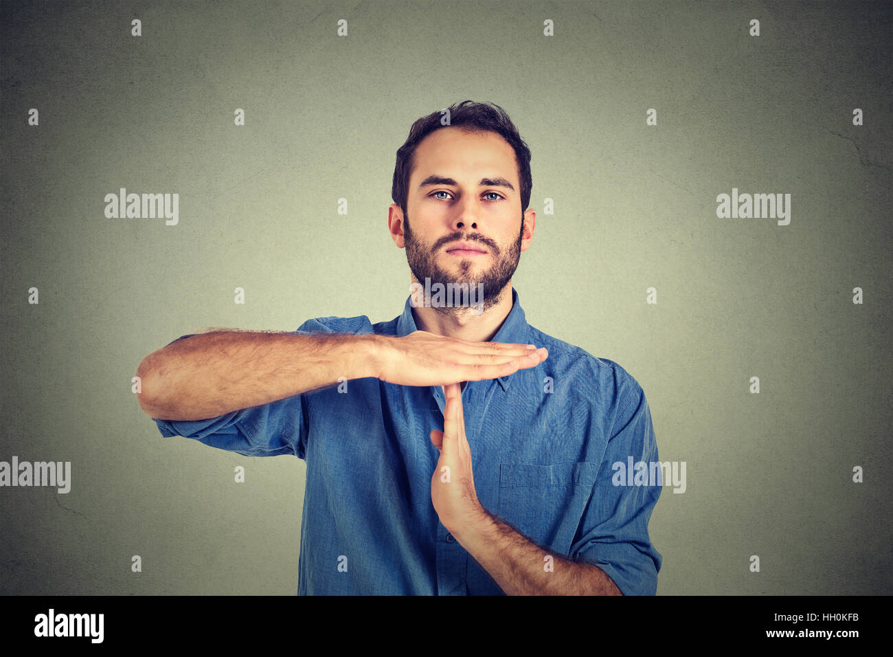 Young man giving showing time out hands gesture isolated on gray wall background Stock Photo