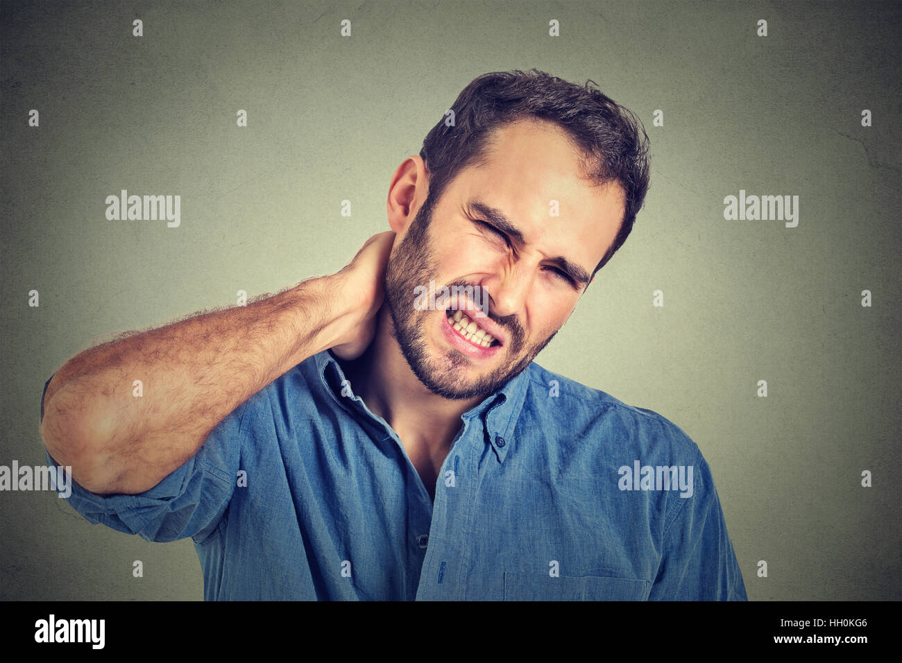stressed, young man with bad neck pain, after long hours of work studying isolated on gray background. Negative human emotion Stock Photo