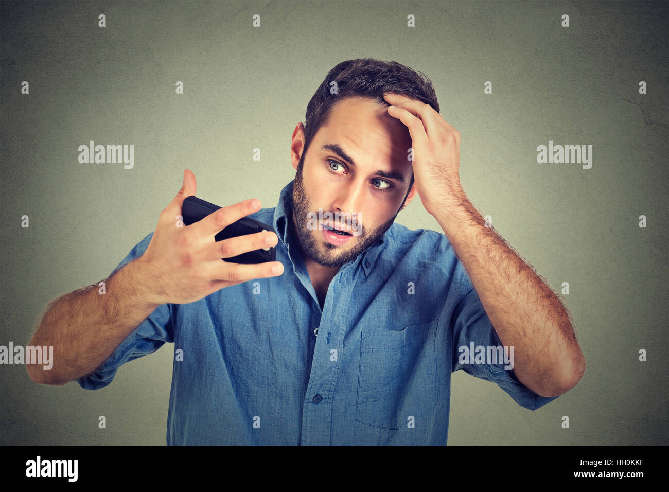 Closeup portrait, shocked man feeling head, surprised he is losing hair, receding hairline, bad news isolated on gray wall background. Negative facial Stock Photo