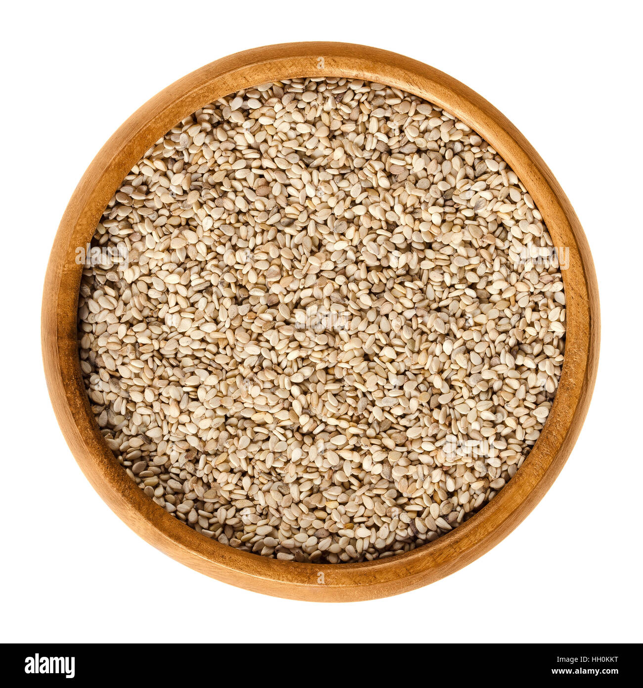 Natural white sesame seeds in wooden bowl. Unpeeled dried fruits of Sesamum, also called benne. Oilseed crops. Isolated macro. Stock Photo