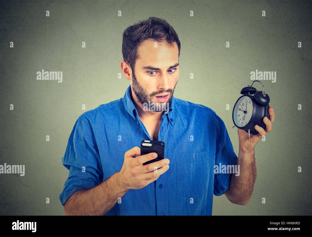 Time management concept. Time is money. Time and new technologies. Portrait perplexed business man with alarm clock looking at smart phone with confus Stock Photo