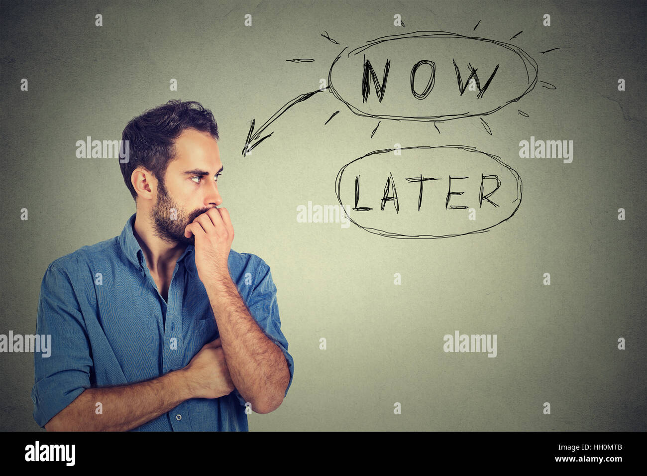 Now or later. Man thinking biting his fingernails looking worried anxious making up his mind isolated on grey wall background. Human face expression Stock Photo